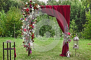 Wedding arch with vinous curtain and fresh flowers outdoors - wedding decoration