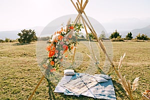 Wedding arch-wigwam stands over homespun bedspreads and pillows on a green meadow in the mountains