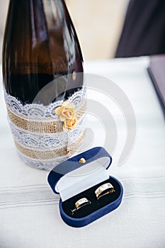 Wedding arrangement on table. Champagne bottle and a box with wedding rings on a white cloth.