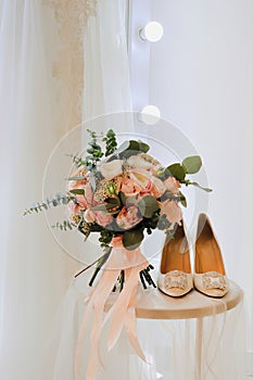 Wedding arrangement: white shoes and bouquet in peach colors standing on round table with mirror and veil aside.