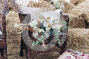 Wedding asymmetrical stylish bouquet with roses on a boho wicker chair.