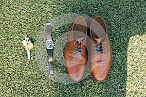 Wedding attributes of the groom: boutonniere, brown shoes and watches on the green grass