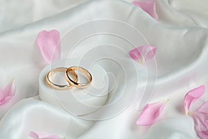 wedding background. gold wedding rings and pink rose petals on white satin fabric. marriage concept.