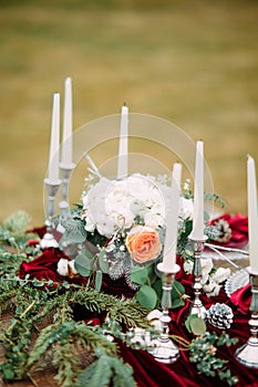 Wedding banquet table with candles, plates, a flower arrangement and a red tablecloth