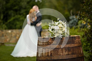 Wedding bouquet on a barrel against the background of the bride and groom at a ceremony in blur