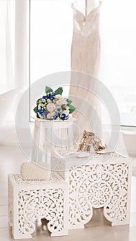 A wedding bouquet, bridal shoes and a pearl clutch stand lie against the background of a white wedding dress. Accessories for