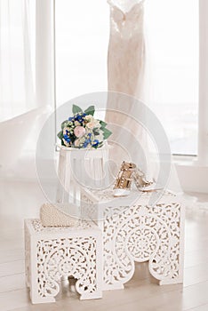 A wedding bouquet, bridal shoes and a pearl clutch stand lie against the background of a white wedding dress. Accessories for