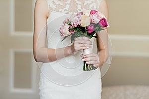 Wedding bouquet in bride`s hands. Slim bride in white dress holding beautiful flowers in hands, going to marry, waiting for her f