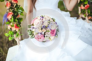 Wedding bouquet close up in hands of the bride on white dress, swing decorated with flowers.