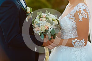Wedding bouquet with delicate pink, beige, white flowers with green leaves in the hands of the brides in dress and costume, couple