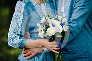 Wedding bouquet flowers from bush roses, eustoma in hands, on the background stylish brides woman wearing embroidered dress and