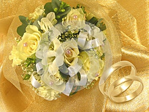 Wedding bouquet with gold wedding rings on golden and white background