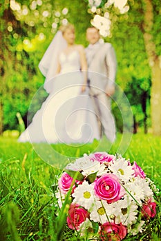 Wedding bouquet on green grass and verry blurred young wedding c