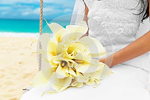 Wedding bouquet lying on the lap of the bride on a tropical beach. Blue sea in the background.