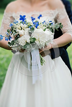Wedding bouquet of peonies, blue flowers and greenery in bride`s hands