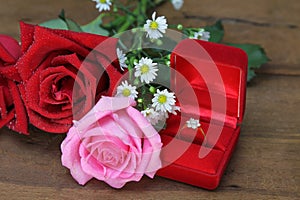 Wedding bouquet from pink and red roses, Wedding ring in a red box on wooden background.