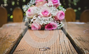 Wedding bouquet with pink roses on wooden table with rings