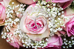 Wedding bouquet with pink roses on wooden table with rings