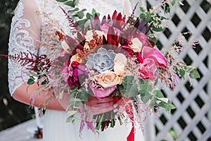 Wedding bouquet with pink tulips, berries and ribbons in hands of the bride