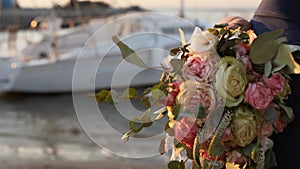 Wedding bouquet of pink, white roses and eucalyptus in bride's hand at the seaside at sunset. Delicate fresh flowers