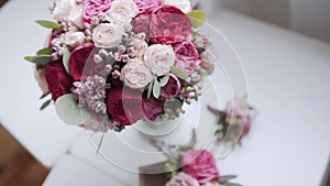 Wedding bouquet of red and pink roses stands in vase on white table, close-up.