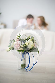 Wedding bouquet from roses with a blue tape costs in a vase. Against the background of newlyweds lie on a bed