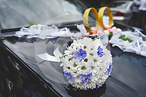 Wedding bouquet of white and blue flowers lies on the bonnet of the car against the background of rings and decor