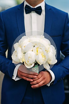 Wedding bouquet of white peonies in the hands of the groom