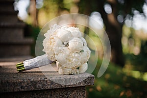 Wedding bouquet of white peonies lies on the marble steps