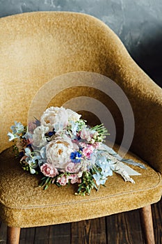 Wedding bouquet in white, pink, blue colors from peonies, roses, cornflowers, bells lies on a mustard-colored armchair