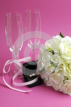 Wedding bridal bouquet of white roses on pink background with pair of champagne flute glasses - vertical.