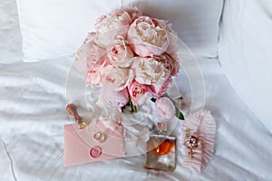 Wedding bride boutonniere, bouquet, perfume and garter laying on white bed linen. Pink bridal flowers and accessories