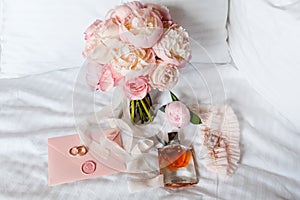 Wedding bride boutonniere, bouquet, perfume and garter laying on white bed linen. Pink bridal flowers and accessories