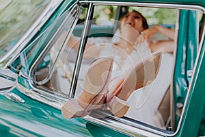 Wedding bride rest and have fun on green vintage retro car after wedding. Honeymoon concept. Car woman happy in old