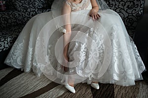 Wedding, the bride in a white dress puts on her beautiful shoes