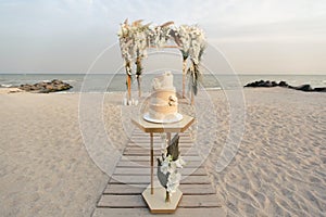 Wedding cake at a beach wedding on the background of a beautiful arch for an exit ceremony.