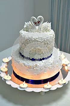 White wedding cake with cream decorated with swans and burning candles