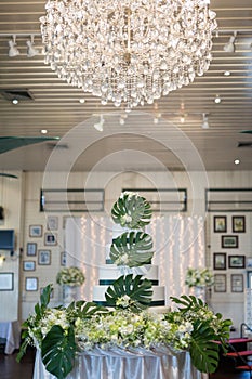 Wedding cake and flowers decorations with chandelier on ceiling.