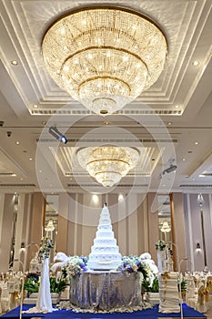 Wedding cake and flowers decorations with chandelier on ceiling.