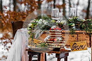 Wedding cake with fruit and an old wooden table with needles of cones and leaves during a wedding ceremony in winter on snow in