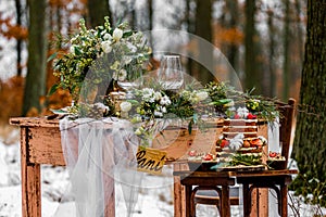 Wedding cake with fruit and an old wooden table with needles of cones and leaves during a wedding ceremony in winter on snow in