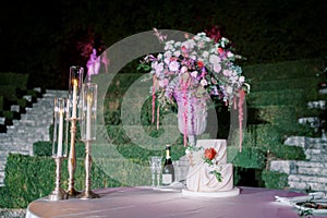 Wedding cake next to a bouquet of flowers and lit candles stands on the table