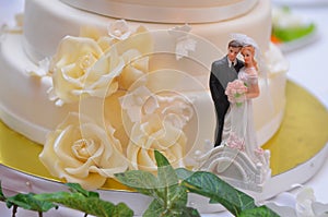 Wedding cake with white cream and beige pink roses with sculptures of the bride and groom on a gold stand