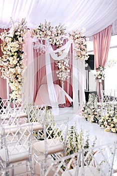 The wedding ceremony area is decorated with white and peach cloth, crystal chandelier, transparent chairs for guests and beautiful