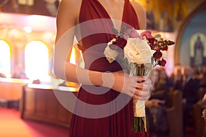 Wedding ceremony day. bridesmaid girl wearing elegant red dress holding flowers bouquet at Wedding ceremony in catholic church.