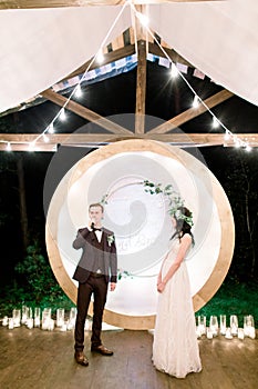 Wedding ceremony in the open air in the stylish rustic wooden tent in forest. Wooden arch with flowers and greenery. The
