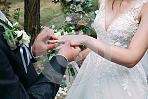 Wedding ceremony of putting on rings to the bride in a white dress and the groom with a boutonniere