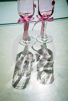 Wedding champagne glasses decorated with pink ribbons, close-up, vertical photo. Wine glasses for the bride and groom