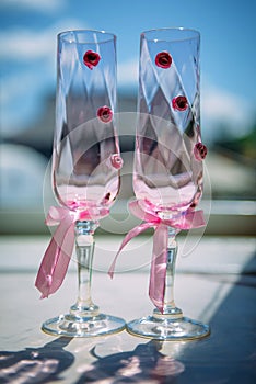 Wedding champagne glasses decorated with pink ribbons and flowers, close-up, vertical photo. Glasses for the bride and groom