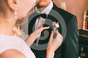 Wedding . Close-up bride`s hands pinning boutonniere to groom`s tuxedo. Warm tones. photo